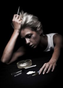 a woman sits in darkness crying while holding needles and opiates